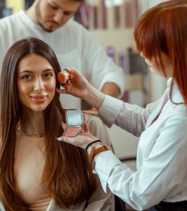 Woman looking at camera, getting professional makeup and hairstyle. Beauty salon services
